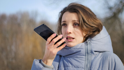 Young girl in blue coat is using her smartphone to send a voice message to a new social network...