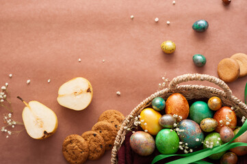 Happy Easter 2021. Colored painted eggs in a wicker basket close-up on a brown background. Easter eggs and sweets. Cookies and chocolate.