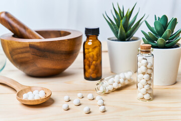 concept of homeopathic pills in a wooden spoon and bottles with a mortar with a pestle on wooden table background          