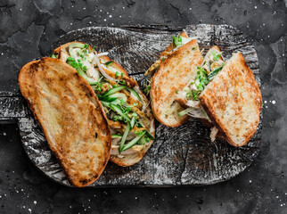 Sandwiches with turmeric fried chicken, cucumber, microgreens and homemade mustard mayonnaise sauce on a wooden cutting board on a dark background. Delicious tapas, snack, breakfast