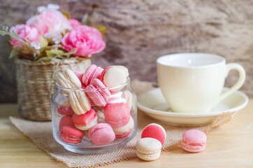 Closed up sweet white and pink macaron over blur soft yellow coffee cup and beautiful rose in wooden basket