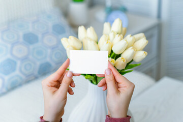 Woman pulling blank greeting card from bouquet of white tulips flowers. Woman day, Copy space. Mock up
