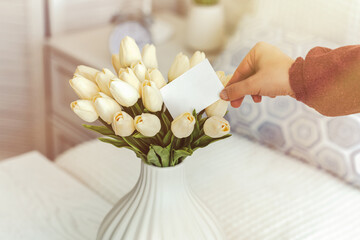 Woman pulling blank greeting card from bouquet of white tulips flowers. Mother day, Copy space. Mock up