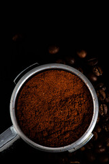 Portafilter with fresh ground coffee on dark background top view