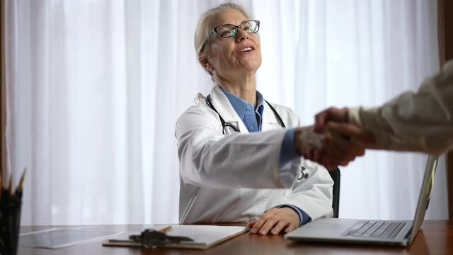 Woman doctor greets a patient with handshake in bright modern office in hospital exam room. Concept of helpful doctor.