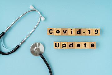 COVID-19 UPDATE text on wooden block. Flat lay view on blue background.