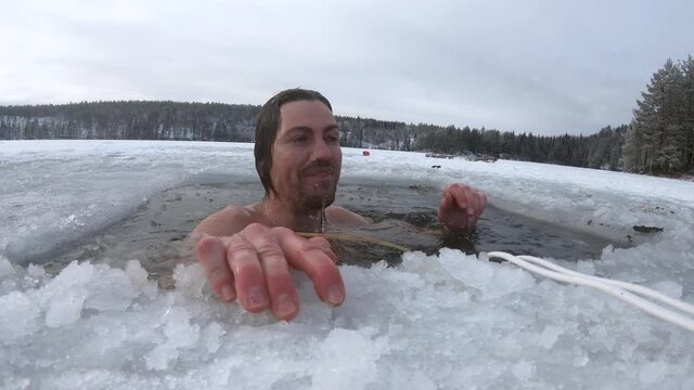 Man swims under the surface of a frozen lake and comes up through a hole cut in the ice