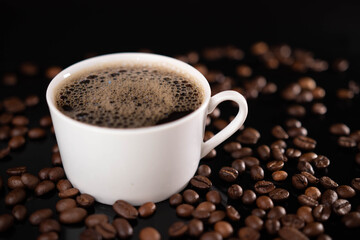 Roasted coffee beans and white mug on black background