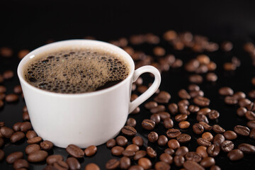 Roasted coffee beans and white mug on black background