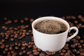 Roasted coffee beans and white mug on black background