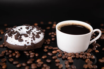 Donut, roasted coffee beans and white mug on black background