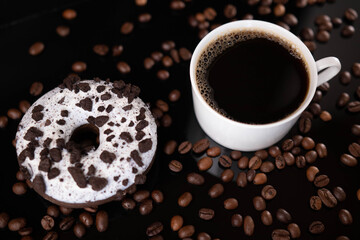 Donut, roasted coffee beans and white mug on black background