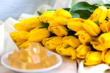 Obraz premium Bouquet of fresh yellow tulips close-up. Flowers in the interior on the background of the bed. Breakfast with coffee and homemade marmalade. The concept of spring and the holiday of March