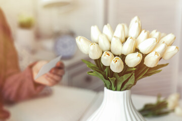 Woman pulling blank greeting card from bouquet of white tulips flowers. Birthday. Sunlight