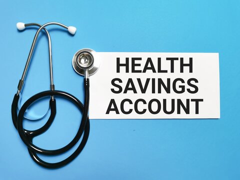 Phrase HEALTH SAVINGS ACCOUNT written on white paper with a stethoscope isolated on blue background. - Powered by Adobe