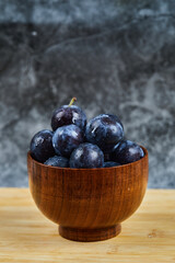 Garden plums in a bowl on wooden table