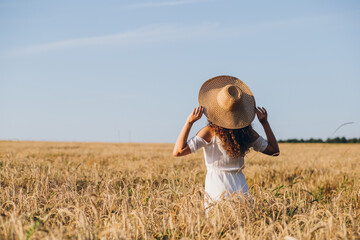 Girl with long curly hair poses in a wheat field