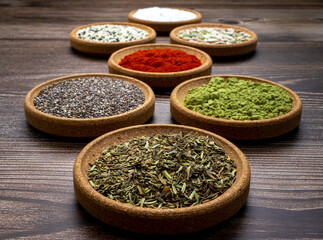 Abstract photography of set of cork tree bowls containing colorful spices, french herbs and seeds on wooden surface and backdrop. 