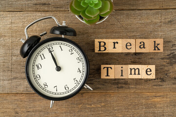 Black vintage alarm clock with a text Break Time on a shabby wooden board background. Flat lay.