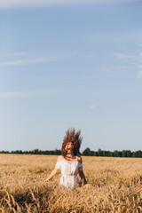 Girl with long curly hair poses in a wheat field