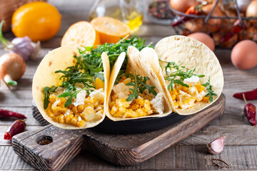 Fresh scrambled eggs with crispy tortillas, cheese, herbs and vegetable on a cutting board on a table