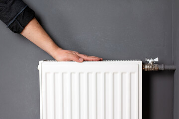 Man warming hands on heating radiator near gray wall