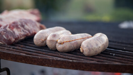 Grilling chorizos in the metal grill outdoor. Closeup view of traditional pork sausages and red meat getting cooked. 