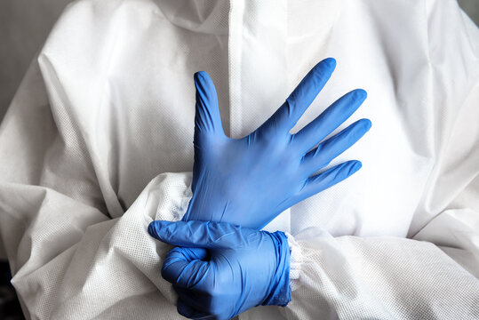 Doctor or nurse in white medical PPE suit puts on protective gloves