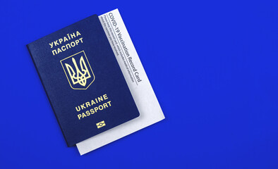 Ukrainian Passport with COVID-19 vaccination record card, vaccination in country on a blue background
