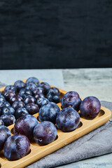 Garden plums on wooden platter and on dark background