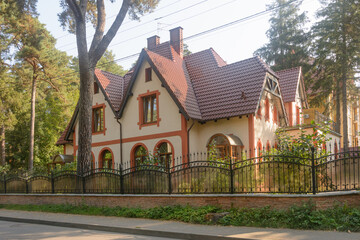 Modern private house with attic floor. Wrought iron fence and large conifers