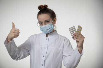 Female doctor in medical mask shows thumb up approving pills, tablets, medicines, advise medication or vitamins