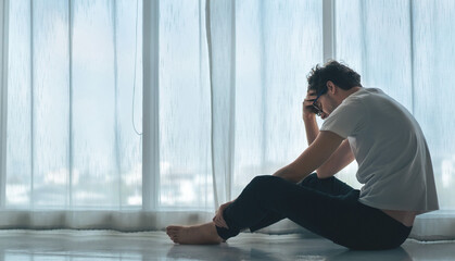 Depressed caucasian man losing job and heartbroken at same time sitting alone near window in dark...
