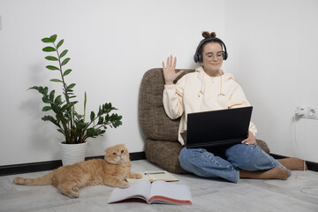 Smiling female student waving hand welcome greeting tutor on distant lesson and remote online class. on laptop sitting with cat at home