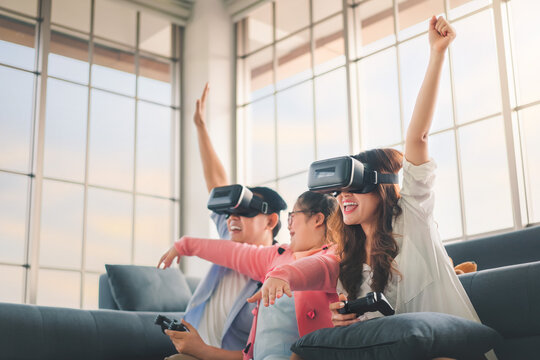 Happy Asian Family  Playing Video Games With VR Headset And Rise Up Hands, With Their Daughter Down Syndrome Child In Living Room, Activity Happy Family Lifestyle Virtual Reality Goggles Concept.