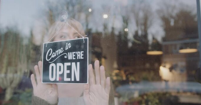 Small business entrepreneur female opening store, turning open sign and look outside for customer