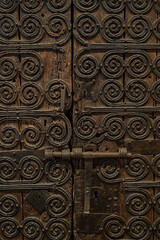 Antigua puerta de madera recubierta de adornos metalicos, con un pestillo metalico que se usa como cierre