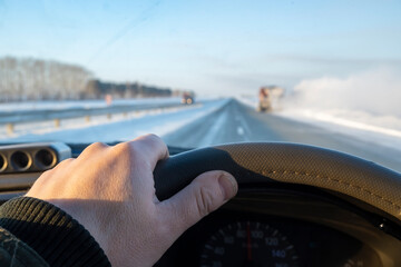 the driver hand is on the steering wheel of a car that is driving on a slippery snow-covered...