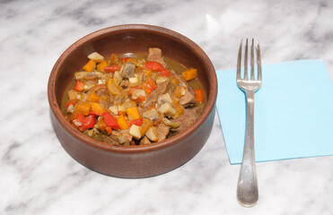 Vegetable stew in an earthenware dish on the table next to a napkin and fork.