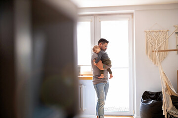 Dad putting to sleep baby boy in his arms at home
