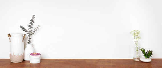 Home decor on a shelf. Vases, succulent plants and branches. Wood shelf against a white wall....