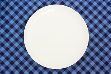 an empty white plate on a blue checkered tablecloth.