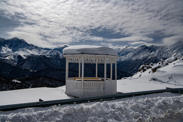 white gazebo for relaxation against the backdrop of snow-capped mountains and blue sky 
