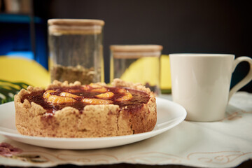 Organic homemade cake with fruits on the white plate with jars and cup. Morning in studio