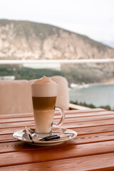 A glass of Latte Macchiato on the terrace of a summer cafe with views of the landscape, mountains and sea, a relaxed morning on vacation