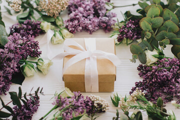 Stylish gift box with lilac and roses flowers on white wood. Happy mothers day and womens day