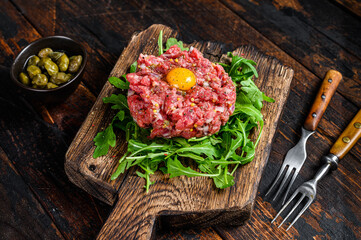 Tartar beef with a quail egg and arugula served on a cutting board. Dark wooden background. Top view