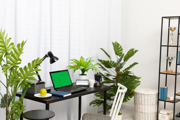 In the house, in the living room, there is a separate space for a workstation with a laptop when working remotely. The laptop is on the black table and right next to it is a coffee mug, a fresh green