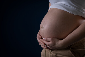 A large, feminine, pregnancy belly on a dark blue background. Hands on the stomach. Ninth month of pregnancy. Blessed state.