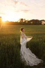 Fototapeta na wymiar Beautiful young bride in lace wedding dress at the field on the sunset